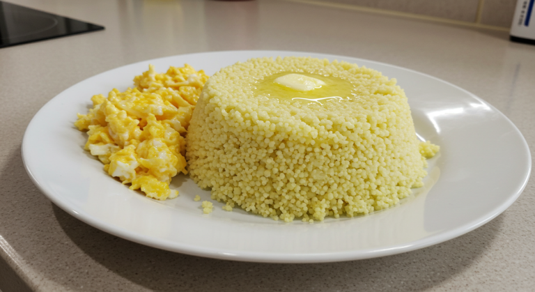 Prato de cuscuz de milho fofinho com ovos mexidos servido em uma bancada de cozinha.