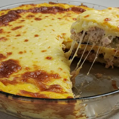 Lasanha de frango super cremosa parcialmente cortada, com queijo derretido se esticando da fatia, servida em uma travessa de vidro sobre uma bancada de cozinha.